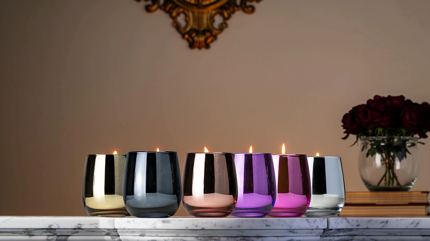 Set of colorful St.Germain glass candle holders on a wooden surface with a decorative wall in the background.